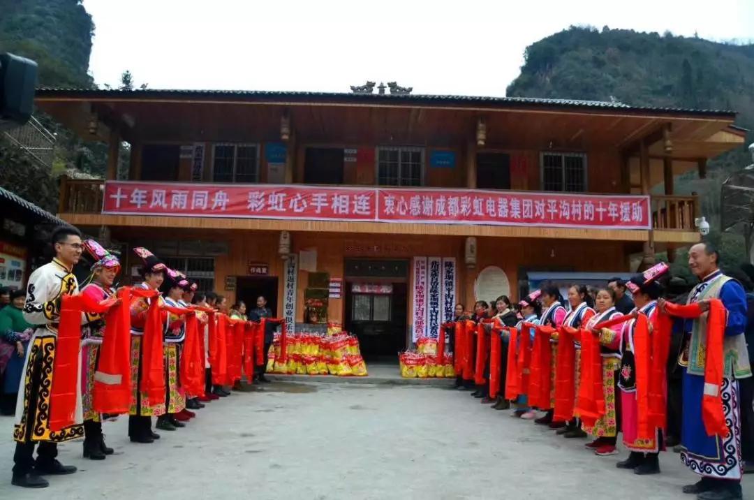 怀感恩之心，平沟村村民手持羌红在乐玩在线手机版（大中国区）公司援建的平沟村便民服务楼前热情等待乐玩在线手机版（大中国区）亲人们的到来